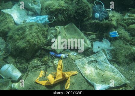 Weggeworfene gebrauchte medizinische Gesichtsmaske zusammen mit anderen Plastikmüll liegt auf dem Meeresboden. Stockfoto