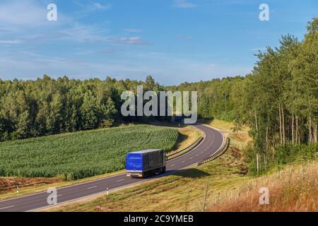 Zwei Lastwagen bewegen sich aufeinander entlang einer Kurve in der Straße in einer ländlichen Gegend, ländlichen Feld, Lkw fahren auf der Straße in der Nähe von landwirtschaftlichen Feldern Stockfoto
