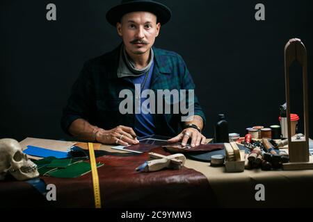 Set von Leder Handwerk Werkzeuge auf Holzhintergrund. Arbeitsplatz für Schuhmacher. Ein Stück Hide und handgeschöpftes Arbeitswerkzeug auf einem Arbeitstisch. Stockfoto