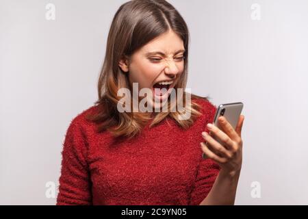 Wütend irritierte Frau den Mund offen halten brüllend wild, schreien, während Blick auf Handy-Bildschirm mit verrückt wütend Ausdruck, aggressive Handy uns Stockfoto