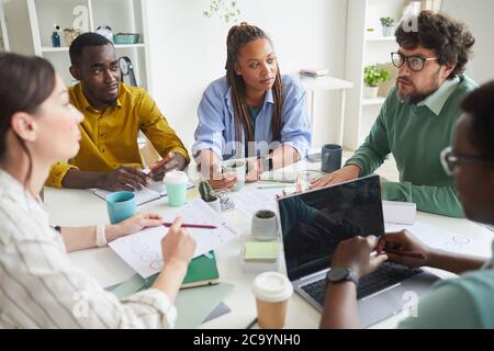 Porträt eines modernen multiethnischen Teams, das Geschäftsprojekt diskutiert, während man an einem überladen Tisch im Konferenzraum sitzt und dem Manager zuhört, um Platz zu kopieren Stockfoto