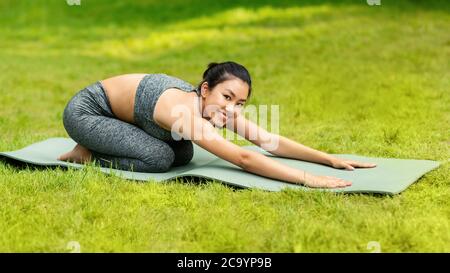 Schöne asiatische Frau macht Kind auf Yoga-Matte im grünen Park posieren Stockfoto