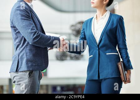 Beschnittenes Bild von ernsthaften jungen Unternehmerinnen und Unternehmerinnen, die die Hände schütteln Stockfoto