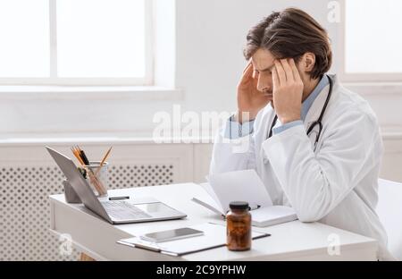 Überarbeiteter männlicher Arzt, der an Kopfschmerzen am Arbeitsplatz leidet Stockfoto