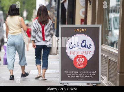 Die Leute passieren ein Schild mit der Werbung für das "Eat Out to Help Out"-Programm, in Covent Garden, London. Ab Montag können die Gäste Mahlzeiten zum halben Preis genießen, da die Regierung ihr August-Programm startet, das darauf abzielt, den Handel mit Restaurants und Pubs nach der Sperre zu fördern. Stockfoto