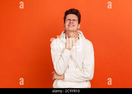 Trauriger Teenager im weißen Kapuzenpullover Grimacing und Schließen der Augen berühren Hals, Gefühl schrecklichen Schmerzen im Hals, Schmerzen beim Schlucken, Mandelentzündung. Studio im Innenbereich Stockfoto