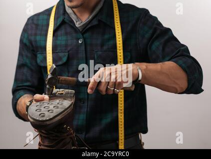 Zugeschnittenes Bild eines Schuhmachers mit Maßband, arbeiten mit der Schuhmacher Mann arbeiten mit Leder mit Basteln hammer Boot, isolierte Schuß über Stockfoto