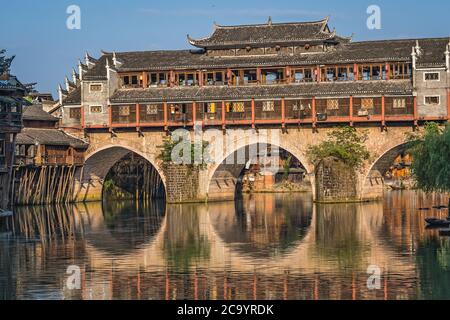 Feng Huang, China - August 2019: Morgendlicher Blick auf die alte historische Bogenbrücke am Ufer des Flusses Tuo, der durch das Zentrum von Fenghu fließt Stockfoto
