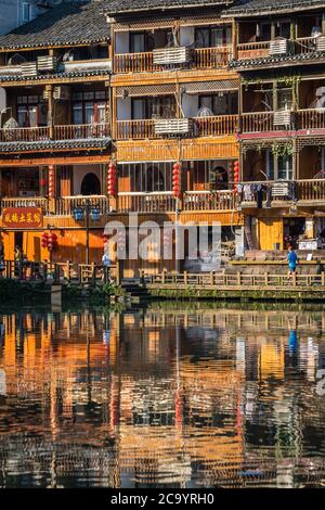 Feng Huang, China - August 2019: Reflexion traditioneller alter Holzhäuser am Ufer des Flusses Tuo, der durch das Zentrum von Feng Huan fließt Stockfoto