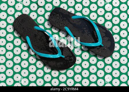 Massagematte für Akupunktur und Schwimmbadflipflops. Grüne und blaue Farbe. Massage zu Hause, Akupunktur-Konzept. Stockfoto