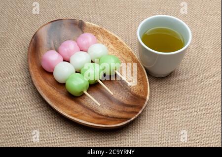 Japanische traditionelle süße Dango Mochi auf Holzplatte mit grünem Tee. Isoliert auf Jute-Hintergrund. Nahaufnahme. Draufsicht. Stockfoto