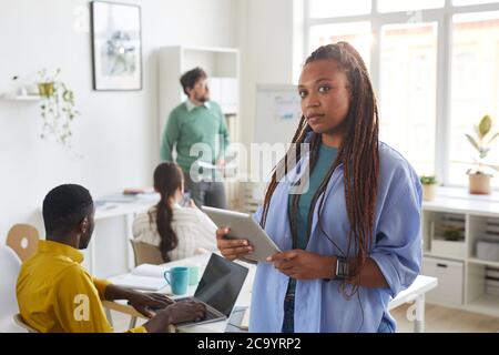 Waist-up-Porträt der zeitgenössischen afroamerikanischen Frau Blick auf die Kamera mit multi-ethnischen Business-Team im Hintergrund, kopieren Raum Stockfoto