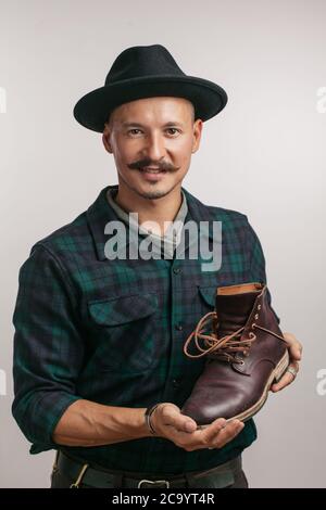 Foto der jungen fröhlichen Schuster in Workshop holding Schuhe. Mit Blick auf die Kamera. Stockfoto