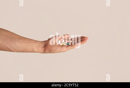 Unerkennbarer junger Kerl hält Haufen Pillen in der Hand über hellen Hintergrund, Nahaufnahme Stockfoto