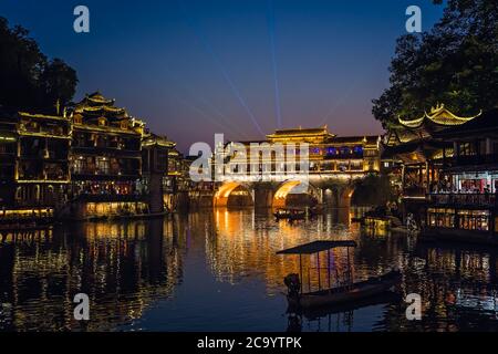 Feng Huang, China - August 2019 : Nachts beleuchtete alte historische Bogenbrücke am Ufer des Tuo Flusses, die durch das Zentrum von Fengh fließt Stockfoto