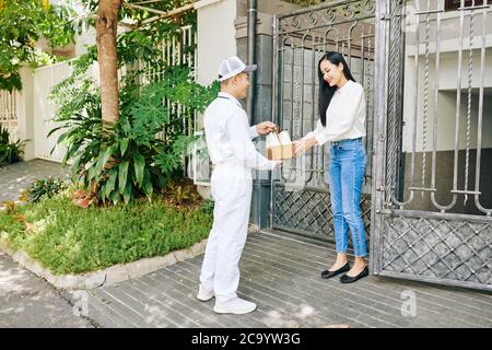 Milchmann gibt Korb mit Glasmilchflaschen an lächelnde vietnamesische Frau Stockfoto