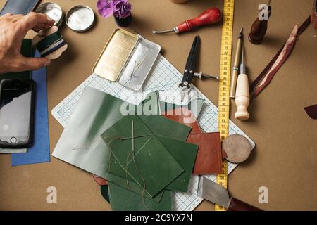 Set von Leder Handwerk Werkzeuge auf Papier Hintergrund. Arbeitsplatz für Schuhmacher. Ein Stück Hide und handgeschöpftes Arbeitswerkzeug auf einem Arbeitstisch. Stockfoto