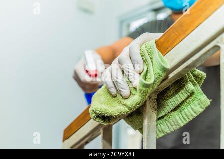 Junger asiatischer Mann in Schutzhandschuhen, der Treppengeländer während der Reinigung zu Hause desinfiziert, Nahaufnahme auf den Händen und mit Sprühflasche. Gesundheitswesen und Stockfoto