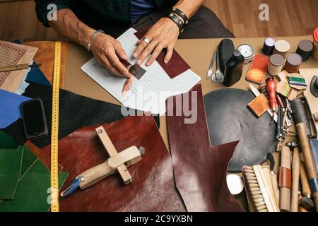 Blick von oben auf die männlichen Schuster Hände halten Schuster Werkzeuge für neue Schuhe in seiner Werkstatt über seinen Arbeitsplatz Hintergrund Stockfoto