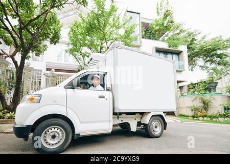 Lächelnder junger vietnamesischer Mann, der Milchwagen fährt und Milchprodukte liefert Stockfoto