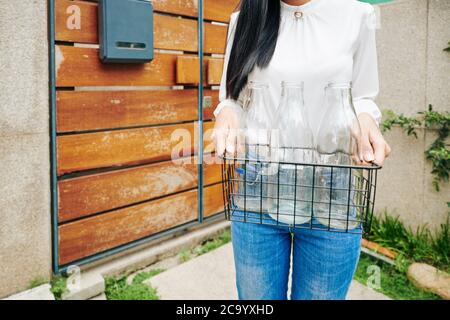 Zugeschnittenes Bild einer jungen Frau, die einen Drahtkran mit leeren Glasflaschen hält Stockfoto