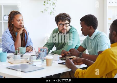 Porträt eines bärtigen, reifen Managers, der mit einem multiethnischen Geschäftsteam spricht, während er Pläne während eines Meetings im Büro diskutiert, Platz kopieren Stockfoto