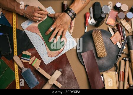 Hohe Winkelansicht des kaukasischen männlichen Handmeisters mit einem Messermuster aus echtem Leder. Herstellung von handgefertigten Lederwaren. Kleinunternehmen Stockfoto