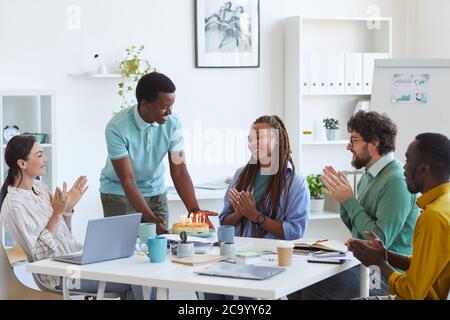 Multiethnische Gruppe von Menschen feiern Geburtstag im Büro, konzentrieren sich auf lächelnde junge Mann bringen Kuchen zu afroamerikanischen Frau, Copy Space Stockfoto