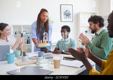 Multiethnische Gruppe von Menschen Geburtstag feiern im Büro, konzentrieren sich auf lächelnde Frau bringen Kuchen zu jungen afroamerikanischen Mann, Copy Space Stockfoto