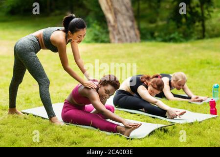 Yogalehrerin, die junge Frau während des Outdoor-Gruppenkursen im Park unterstützt Stockfoto