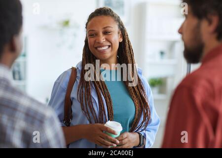 Waist-up-Porträt der zeitgenössischen afroamerikanischen Frau lächelt glücklich, während im Gespräch mit Freunden oder Kollegen drinnen, kopieren Raum Stockfoto