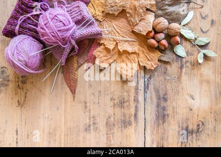 Gestrickte Socke, Garnknäuel und Stricknadeln auf rustikalem Tisch. Wollstrick, Blätter und Nüsse auf Vintage-Holzfläche. Draufsicht. Speicherplatz kopieren. Kalt Stockfoto