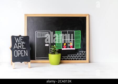Haus Zeichnung auf Tafel, Pflanze in Topf und WIR SIND OFFENES Wort auf Tafel. Offenes Singboard in der Nähe des Hauses, auf Tafel gezeichnet. Open Small Business Konz Stockfoto