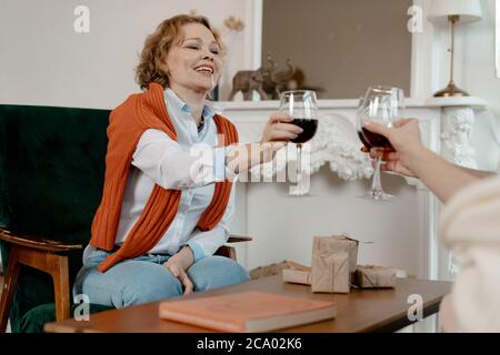 Alte Freunde Trafen Sich Im Stilvollen Wohnzimmer Und Trinken Wein. Happy Smiling Senior Blonde Frau gibt EINEN Toast über Frau Freundschaft. Natürliche Alterung Stockfoto