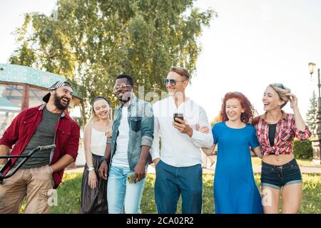 Gruppe von glücklichen multirassischen Kollegen tragen stilvolle Kleidung gehen auf die Outdoor-Körperparty im Park am sonnigen Sommertag. Freizeit, Urlaub, Stockfoto