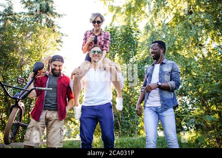 Gruppe von glücklichen multirassischen Kollegen tragen stilvolle Kleidung gehen auf die Outdoor-Körperparty im Park am sonnigen Sommertag. Freizeit, Urlaub, Stockfoto