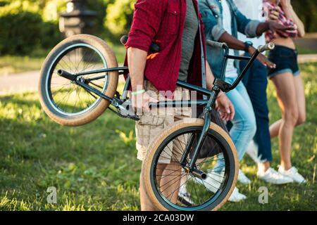 Nicht erkennbarer Mann mit BMX Byke Nahaufnahme zu Fuß zusammen mit seinen Freunden im Park. Menschen, Extremsport, Fun-Konzept Stockfoto