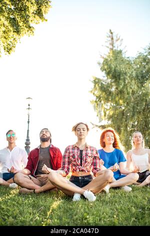 Zeit für Yoga. Konzentrierte junge Freunde meditieren in Yoga-Lotusposition, während sie sich nach einer langen Reise im Botanischen Garten ausruhen. Multiethnische Menschen dr. Stockfoto