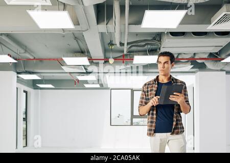 Portrait von nachdenklichen jungen Kopf Ingenieur Inspektion Gebäude im Bau und Notizen in Dokument auf Tablet-Computer Stockfoto