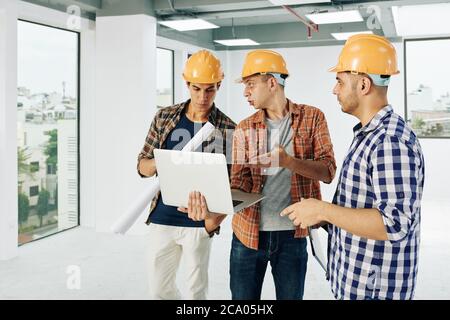 Team von seriösen jungen Ingenieuren in Hartmützen diskutieren Gebäude Anlage auf Laptop-Bildschirm Stockfoto