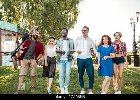 Gruppe von glücklichen multirassischen Kollegen tragen stilvolle Kleidung gehen auf die Outdoor-Körperparty im Park am sonnigen Sommertag. Freizeit, Urlaub, Stockfoto