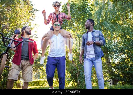 Gruppe von glücklichen multirassischen Kollegen tragen stilvolle Kleidung gehen auf die Outdoor-Körperparty im Park am sonnigen Sommertag. Freizeit, Urlaub, Stockfoto