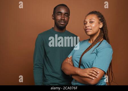 Minimal Taille up Porträt des modernen afroamerikanischen Paar Blick auf die Kamera, während souverän vor braunem Hintergrund im Studio stehen, kopieren Raum Stockfoto