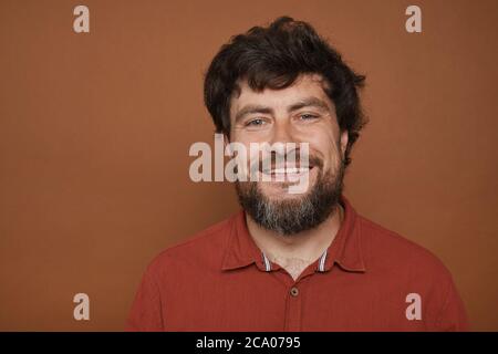 Minimal Kopf und Schultern Porträt von reifen bärtigen Mann lächelt an der Kamera, während vor braunem Hintergrund im Studio stehen, kopieren Raum Stockfoto