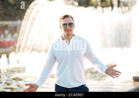 Porträt eines jungen selbstbewussten Mannes, der in seiner Freizeit allein in der Sommerstadt unterwegs ist, in legerer Kleidung und Schutzbrille Stockfoto