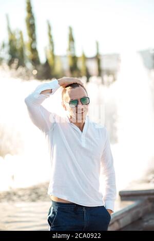 Porträt eines jungen selbstbewussten Mannes, der in seiner Freizeit allein in der Sommerstadt unterwegs ist, in legerer Kleidung und Schutzbrille Stockfoto