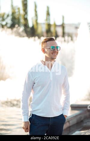 Porträt eines jungen selbstbewussten Mannes, der in seiner Freizeit allein in der Sommerstadt unterwegs ist, in legerer Kleidung und Schutzbrille Stockfoto