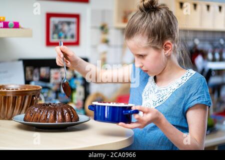 Junge Mädchen in blauen T-Shirt macht, einfach zuzubereiten und gesund, hausgemachte Osterkuchen. Sie schmückt den Kuchen mit dunkler Schokolade. Stockfoto