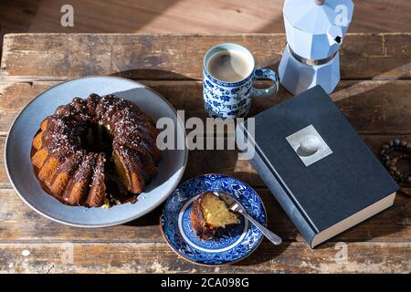 Leckeres Stück Osterkuchen, gutes Buch und heißer Kaffee auf altem, dunklem Holztisch - schöner Nachmittag während des Aufenthalts zu Hause. Stockfoto