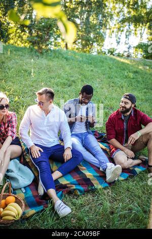 Gruppe von multirassischen Freunden in legerer Sommerkleidung mit Smartphone gekleidet Spaß zusammen im Park, beobachten lustige Videos in sozialen Medien. Stockfoto